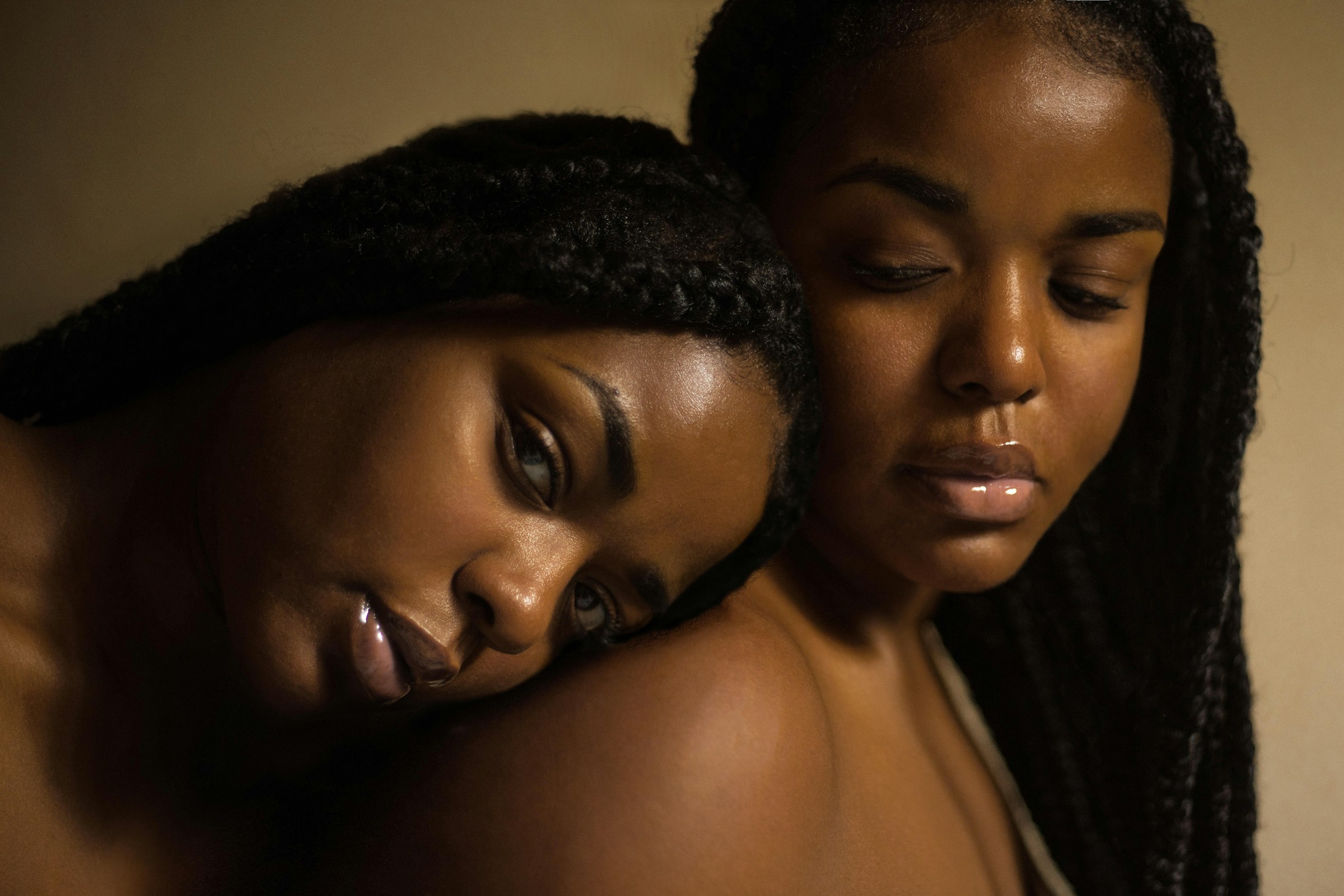 Two women, one rests her head on the shoulder of the other who is looking down.