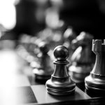 A black and white image of a chess board, taken from one corner so that the black pawn is in focus while the rest of the image is blurred.