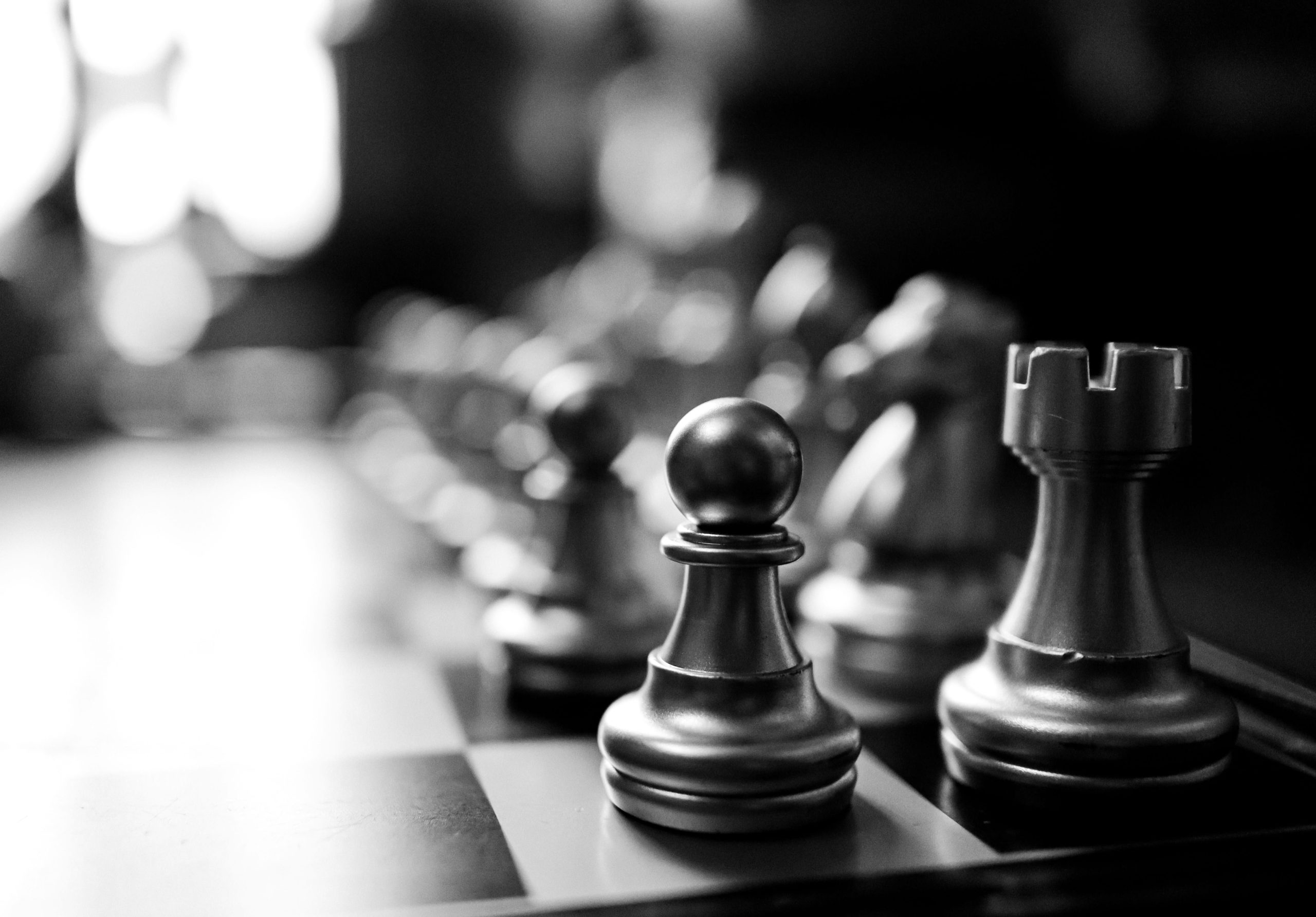 A black and white image of a chess board, taken from one corner so that the black pawn is in focus while the rest of the image is blurred.